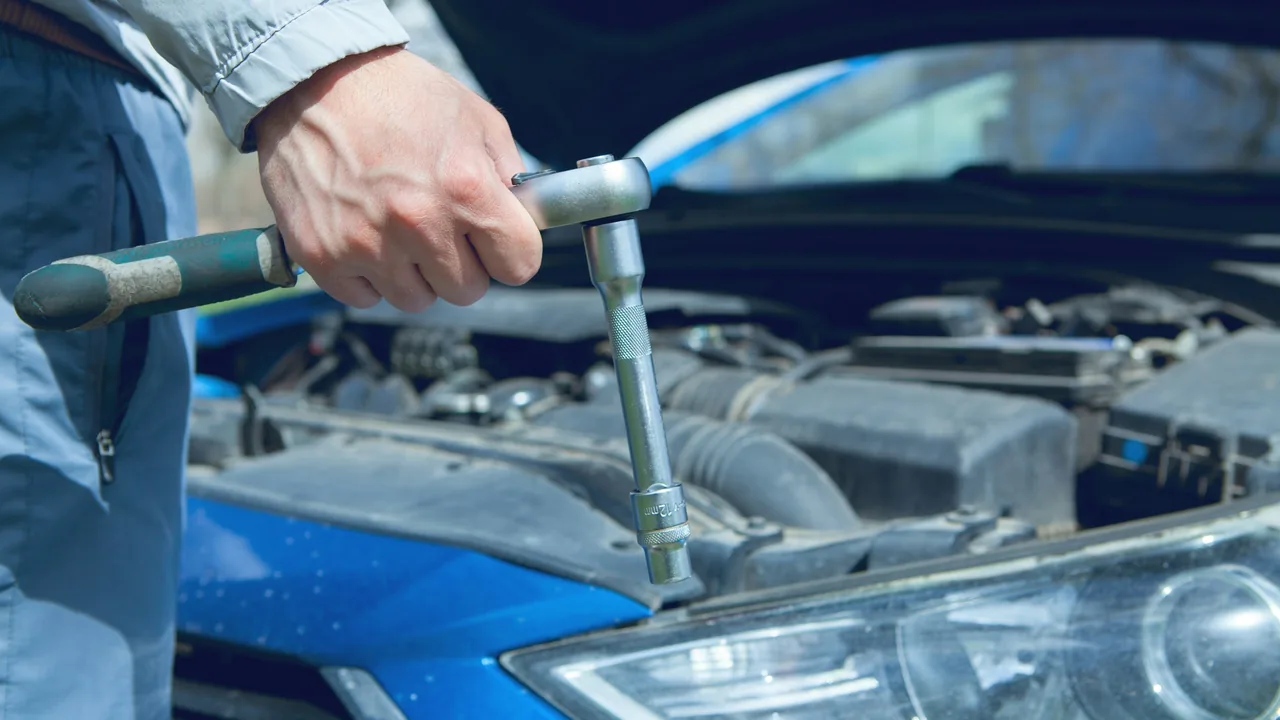 A hand holding a socket wrench over an open car engine bay