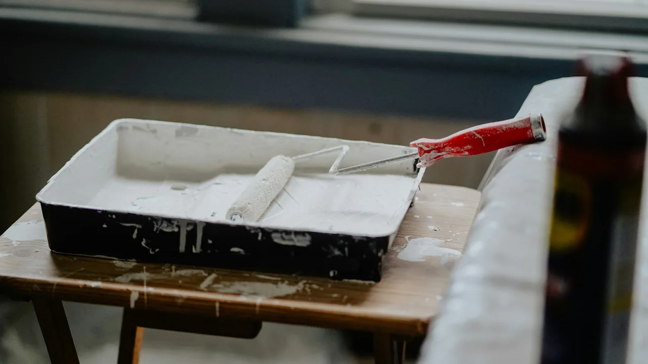 White paint roller with a red handle resting in a paint tray